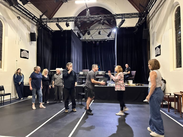 Group of people standing and conversing on a theatre stage during an interview or rehearsal session.