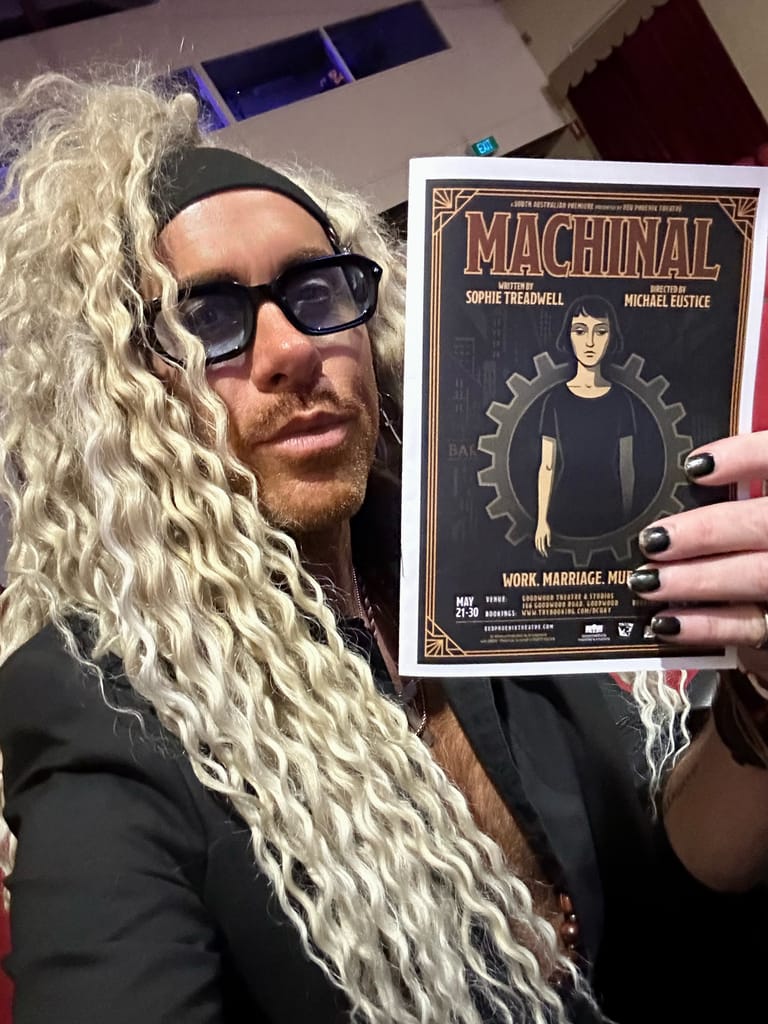Person wearing sunglasses and long blonde wig holds a Machinal theatre production programme featuring geometric art deco design.