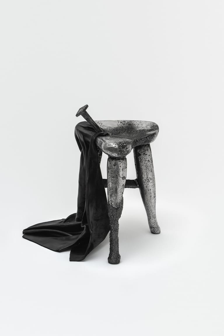 Wooden stool with hammer and black fabric draped across it against a white background.