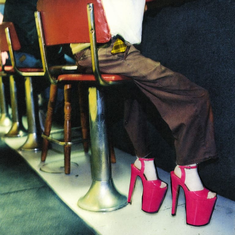 Performer's feet in bright pink platform heels resting on stage beside a brass instrument during a new music performance.