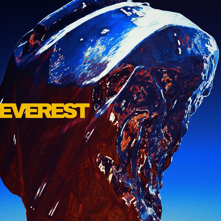 Large sculptural head with blue and burgundy glazed surface against clear sky, "EVEREST" text visible.