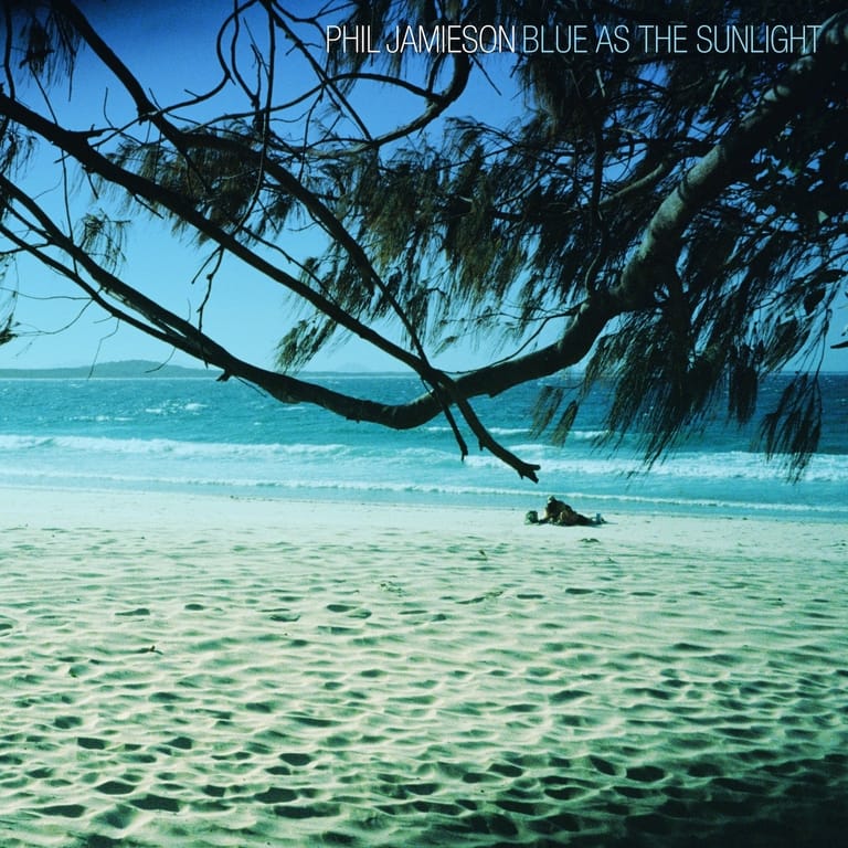 Tropical beach with turquoise waters and drooping tree branches framing a distant solitary figure.