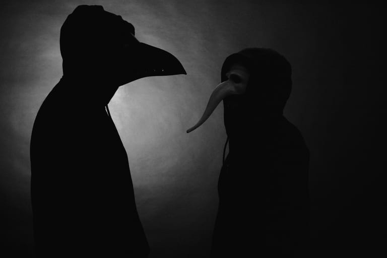 Two silhouetted figures with elongated beaked profiles face each other against a grey, atmospheric background.