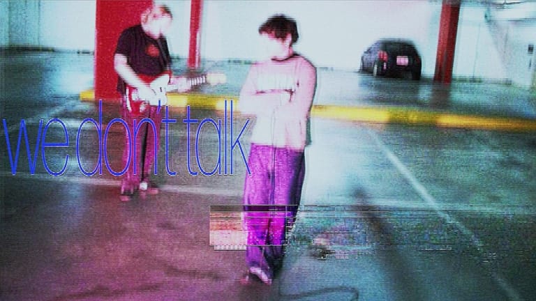 Two figures stand in a neon-lit carpark under red and blue lighting, with glitchy digital effects overlaid across the scene.
