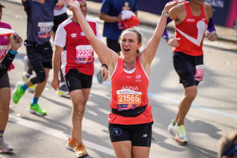 Runner in red bib celebrates with arms raised while participating in a community running event.