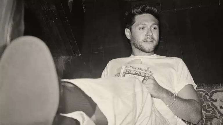 Man in a cream t-shirt seated in a vehicle, looking toward the window in black and white photography.