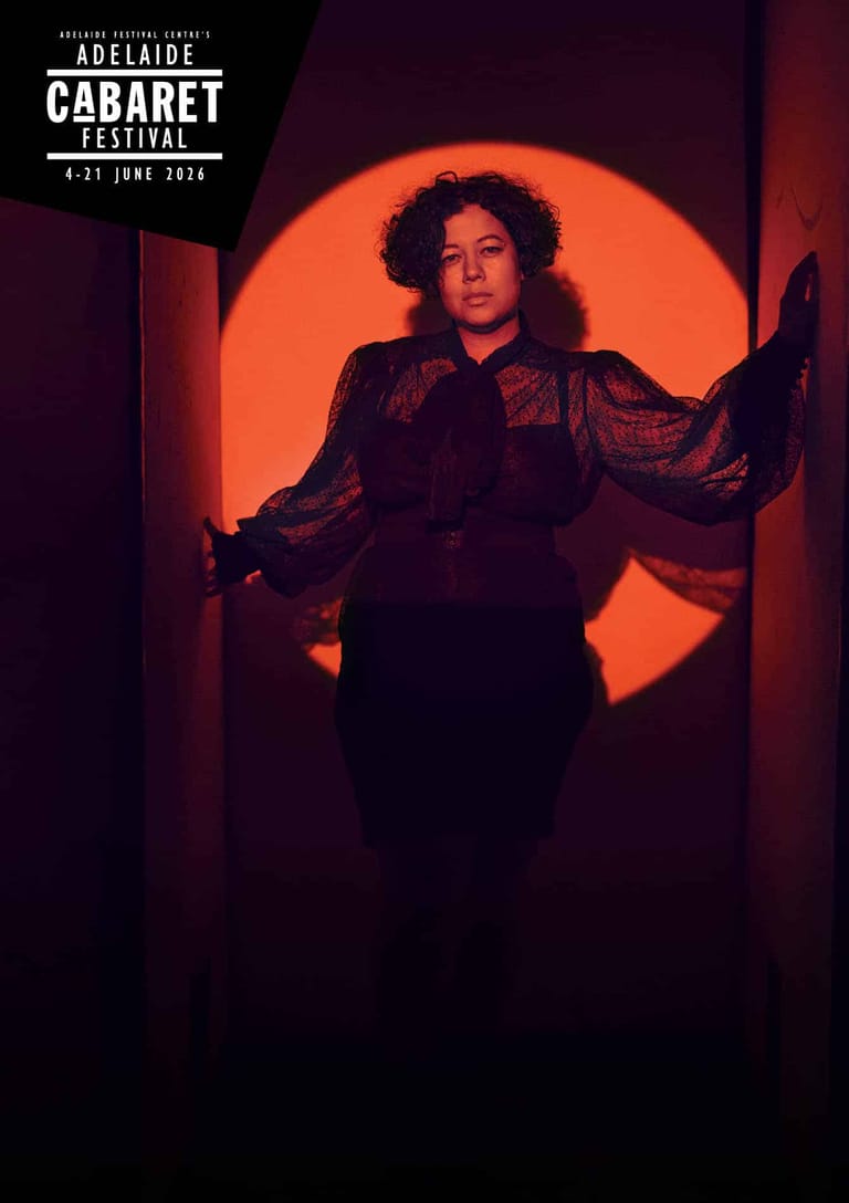 Singer in textured jacket silhouetted against a large glowing orange circle during a cabaret performance.