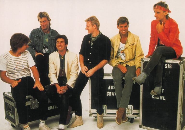 Six musicians seated and standing on amplifiers against a white background during a band photoshoot.