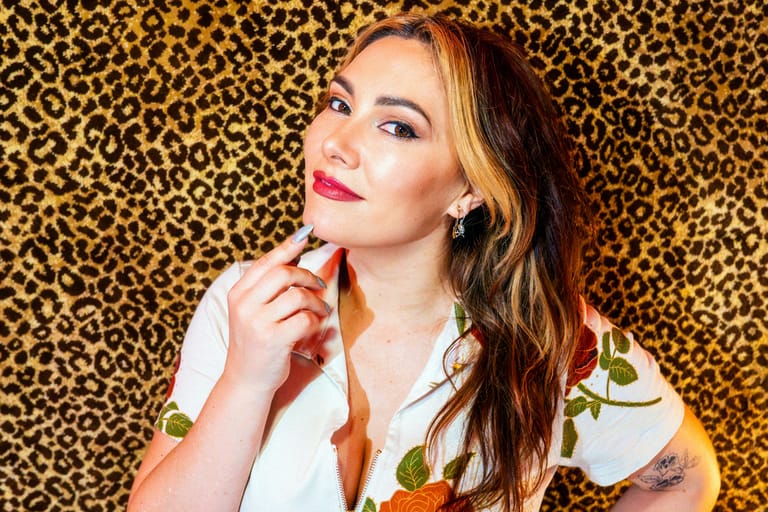Woman with long brown hair and pink lipstick poses against a leopard-print backdrop.