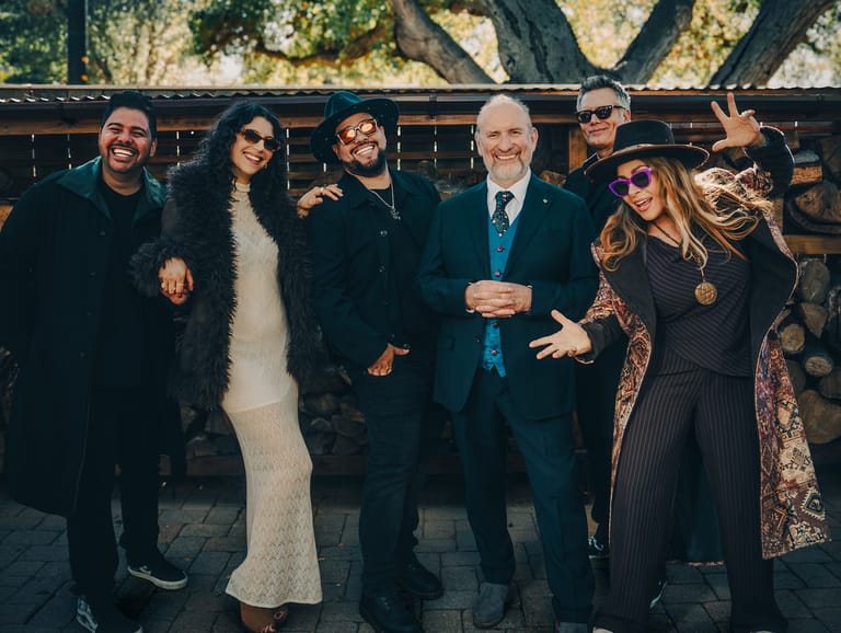 Six people in formal black and blue attire stand together outdoors against a wooden fence backdrop.