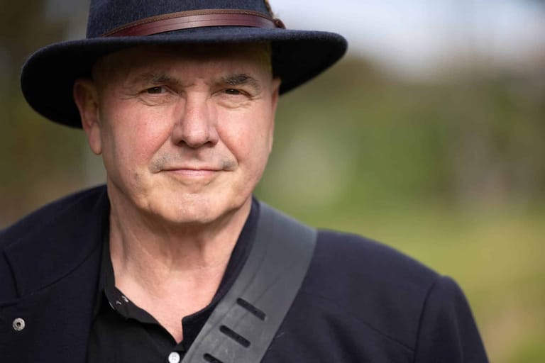 Man in dark shirt and cowboy hat with guitar strap, blurred green background.