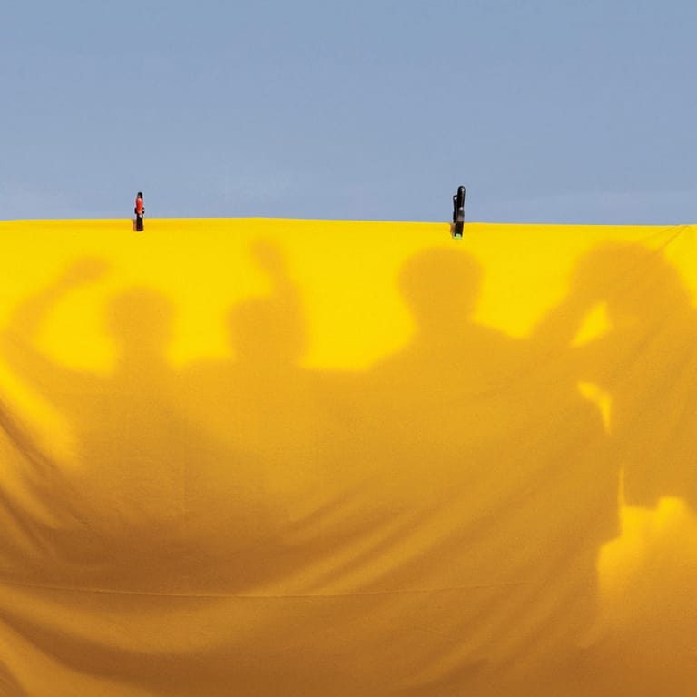 Two figures stand atop a vast yellow inflatable structure against a clear blue sky.