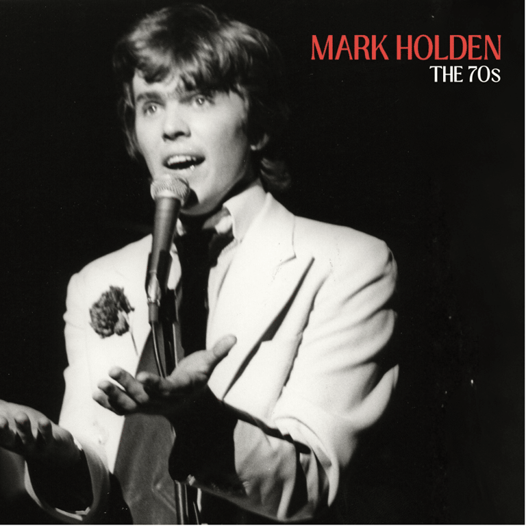 Man in light suit singing at microphone against black background, black and white photograph.