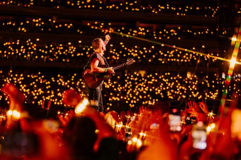 Performer on stage surrounded by thousands of glowing lights held by audience members during an evening concert.