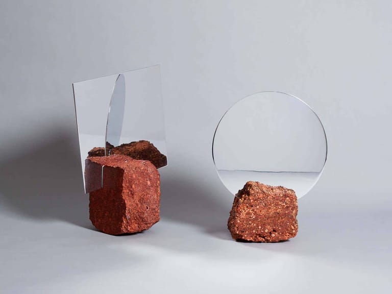 Two rust-coloured textured blocks with glass vessels balanced on top against a neutral background.