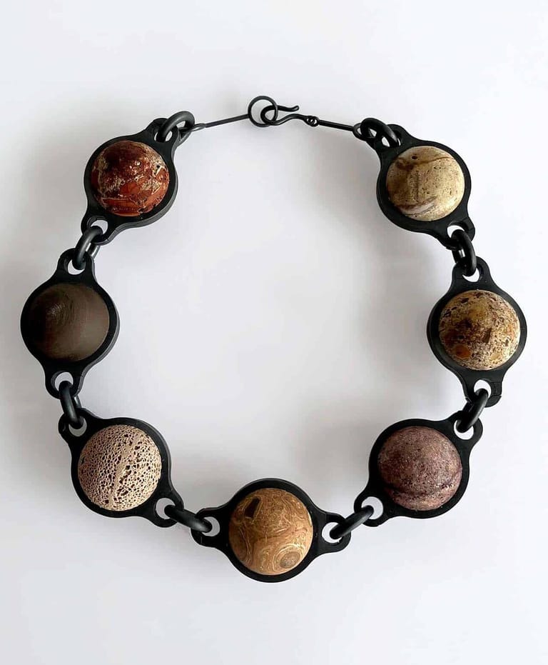 Black metal bracelet with seven circular resin pendants in varying earth tones and textures, displayed against a white background.