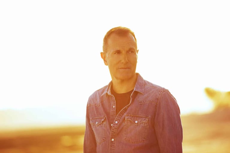 Man in dusty pink shirt standing in golden sunlit landscape.