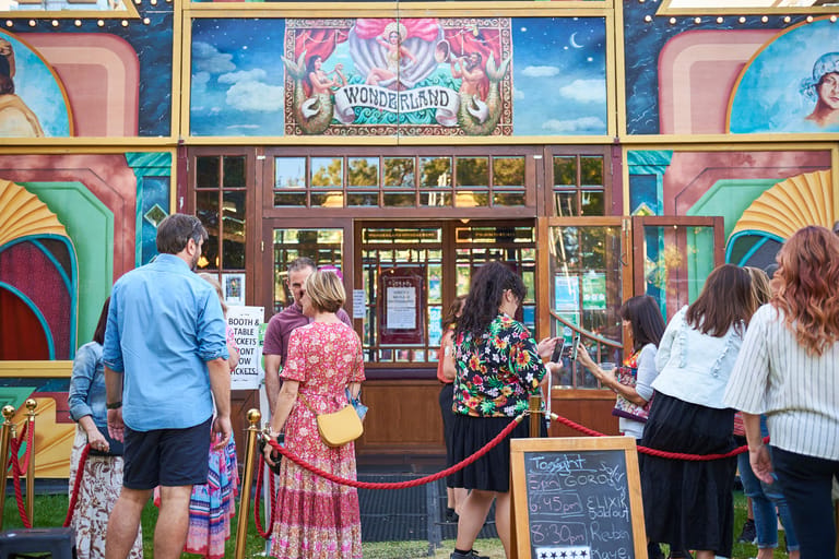 Colourful vintage-style shopfront with customers gathered outside, featuring ornate signage and hand-painted murals.