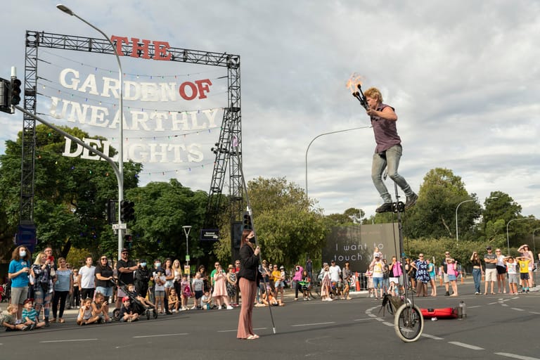 Performer on a unicycle launches into the air during an outdoor street performance at the Garden of Unearthly Delights festival.