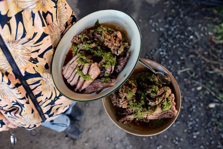 Two bowls of beef noodle soup with fresh herbs served on a patterned cloth, viewed from above.