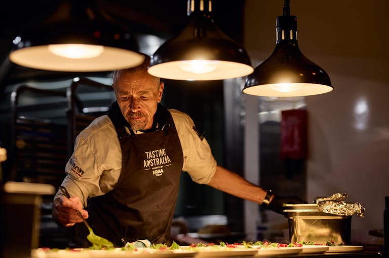 Chef in apron stands at counter under pendant lights, preparing food in professional kitchen setting.