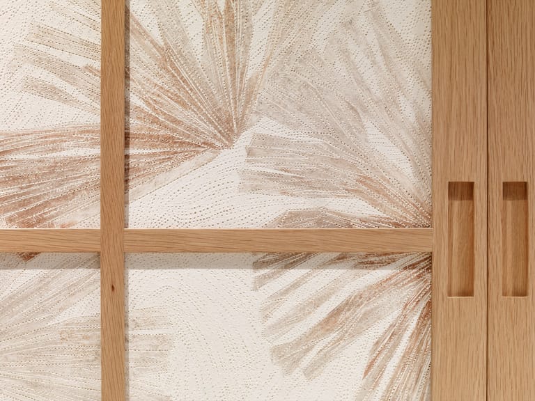 Sunlight casts leaf shadows across a wooden-framed window and door in warm, neutral tones.