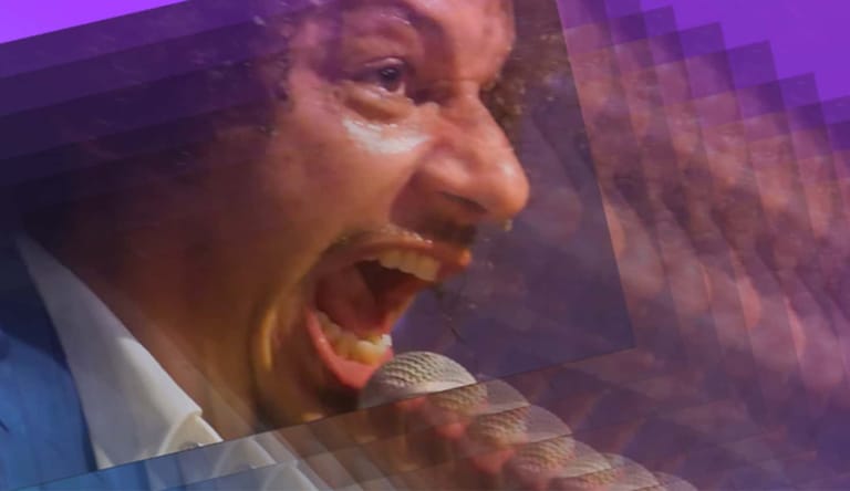 Singer performing at a microphone under purple stage lighting with an animated expression.