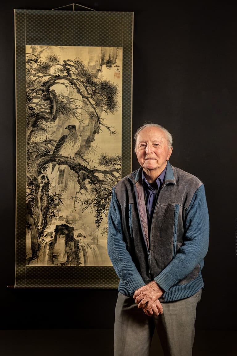 Man standing beside a traditional East Asian landscape scroll painting on a dark background.