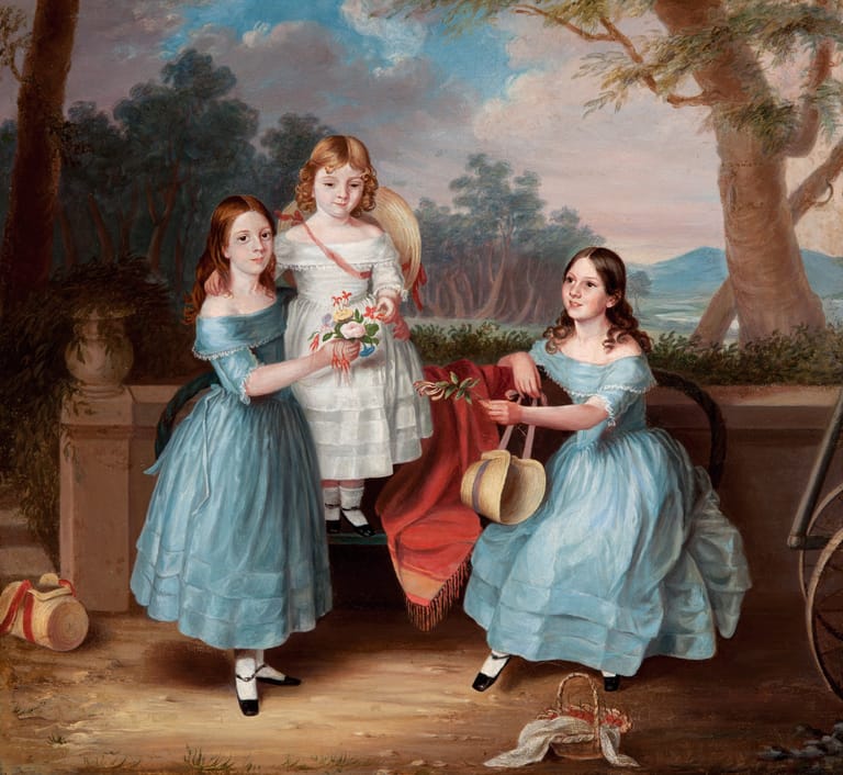 Three young girls in blue and white dresses pose in a classical garden setting, one holding flowers and another with a musical instrument.