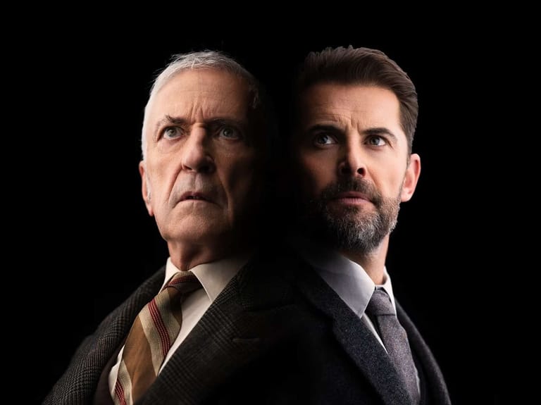 Two men in business suits posed against a black background.