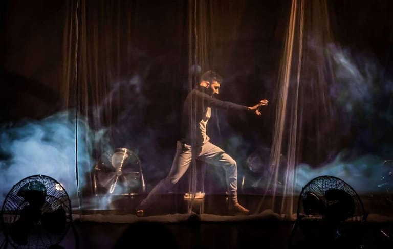 Performer suspended in aerial silks against dramatic blue smoke and stage lighting during a circus production.
