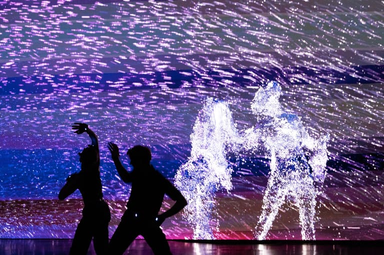 Silhouetted figures interact with glowing digital projections in an immersive purple and blue-lit installation.