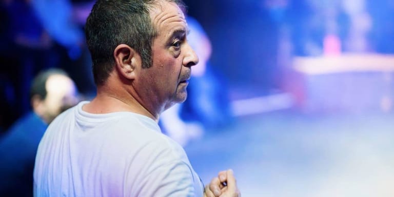 Man in white shirt speaking or performing on stage under blue stage lighting.