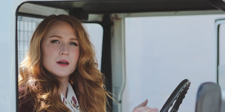 Woman with auburn wavy hair seated in a vehicle, gazing thoughtfully to the side.