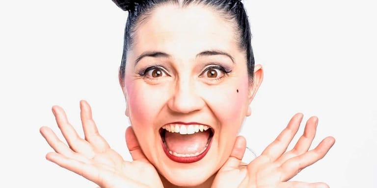 Woman with hands raised to face, smiling broadly with red lips against white background.