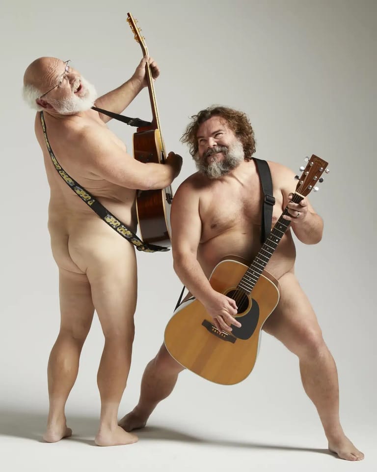 Two bare-chested men pose playfully with acoustic guitars against a neutral background.