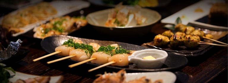 Grilled skewers and seafood dishes arranged on a dark table with dipping sauce and fresh herbs.
