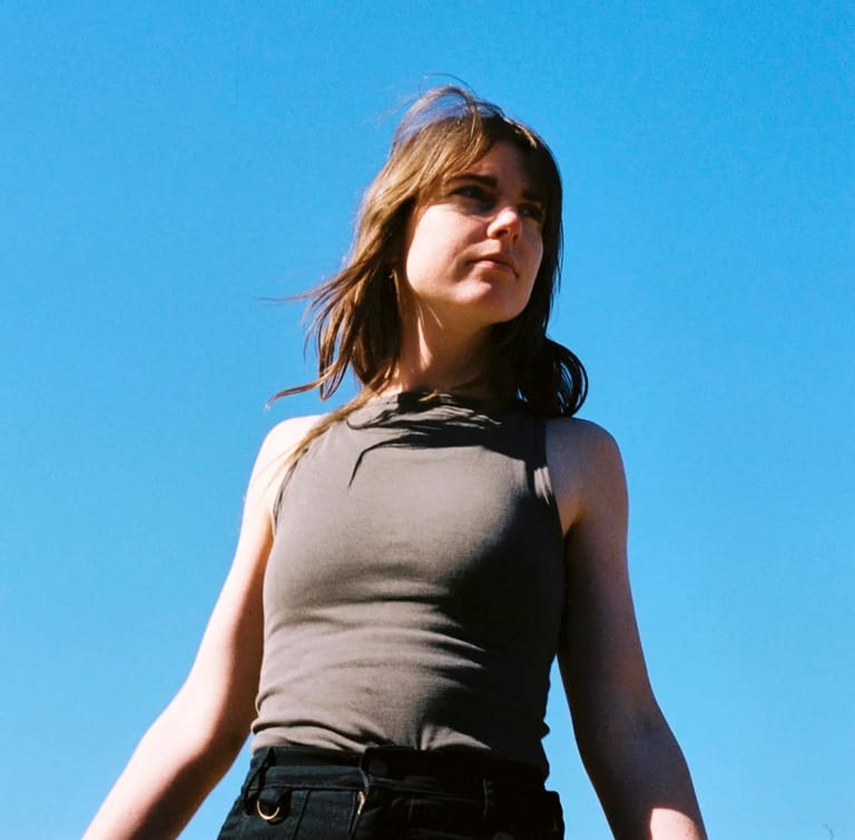 Person in grey sleeveless top and black jeans standing against clear blue sky.