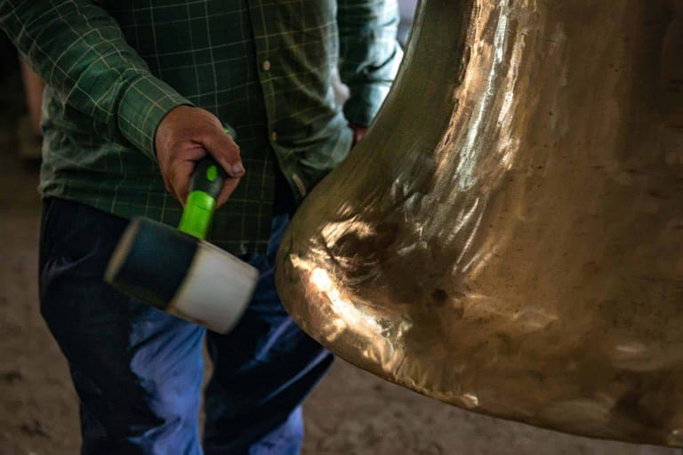 Person in green shirt holding a bright green tool against a large bronze sculptural form.
