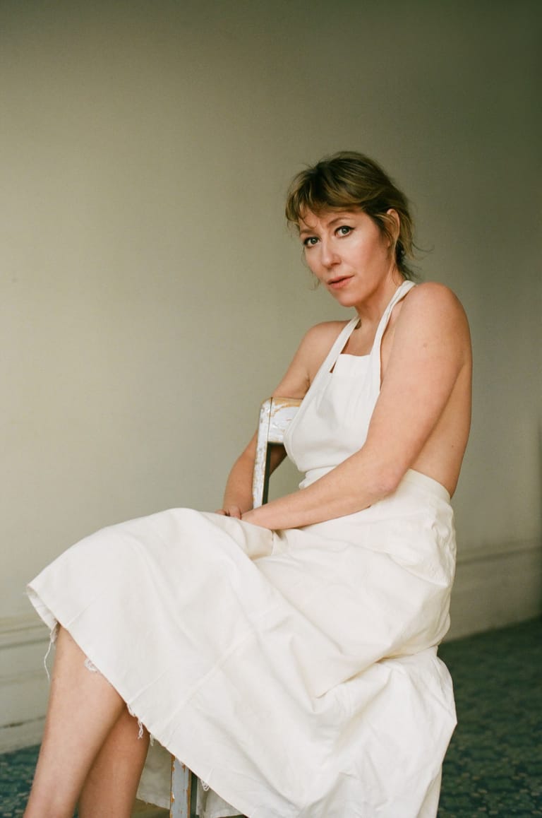 Woman in a white halter dress seated against a neutral backdrop, looking toward the camera.