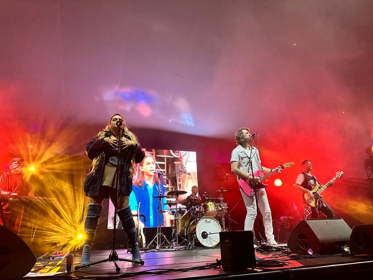 Band performs on stage bathed in red and yellow spotlights during a 90s-themed concert production.