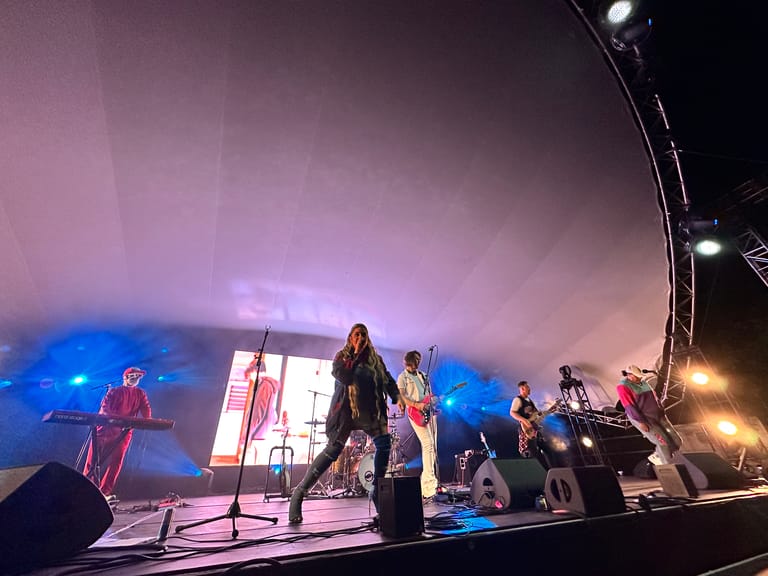 Band performs on stage bathed in pink and blue lighting during a 90s-themed concert production.