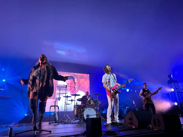 Band performing on stage under blue and pink spotlights during a 90s-themed show production.
