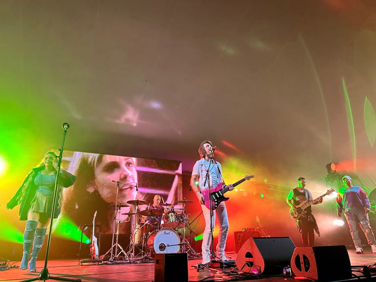 Band performing on stage under coloured lighting during a 90s-themed concert production.