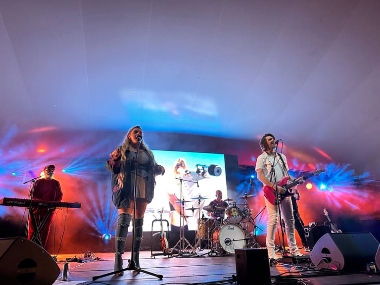 Band performing on stage with colourful blue and orange lighting during a 90's-themed show production.
