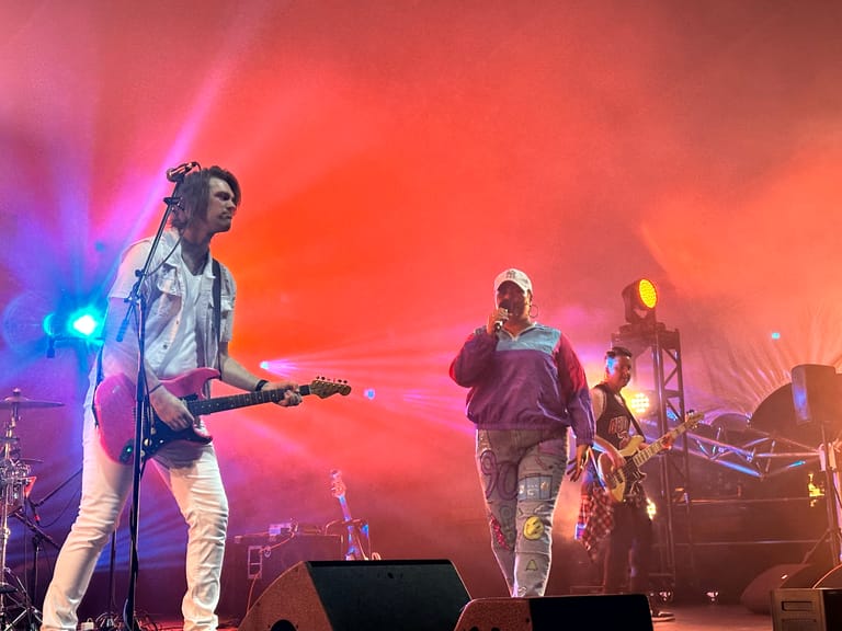 Band performs on stage bathed in red and blue lighting during That 90's Show concert.