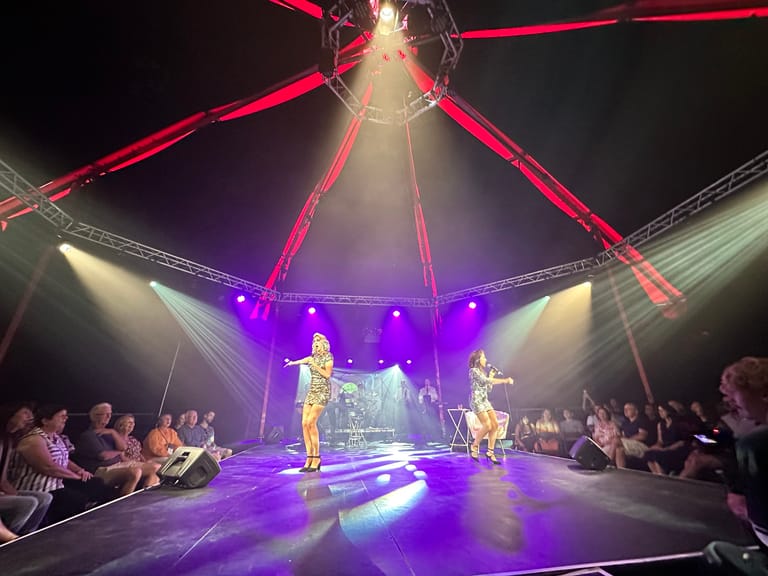 Young performers in vintage-style costumes perform under dramatic purple and red stage lighting in a tent venue.