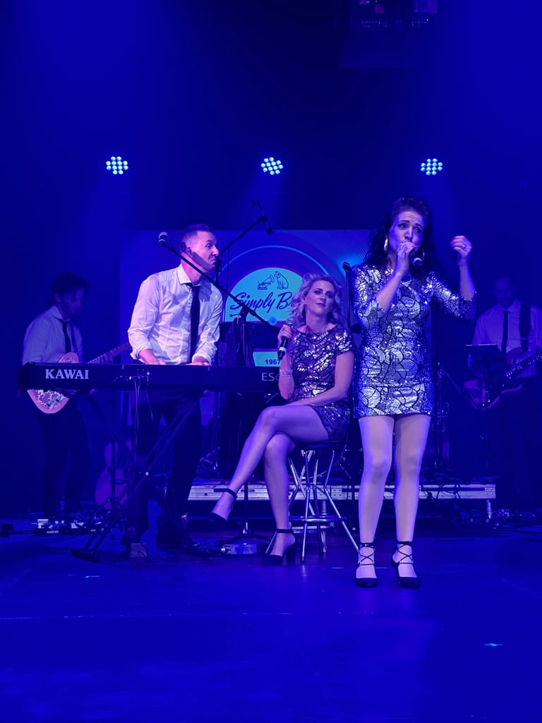 Young performers on stage under blue lighting during a 1960s rock and roll tribute production.