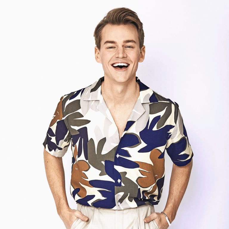 Man in a bold geometric patterned shirt smiling against a neutral background.