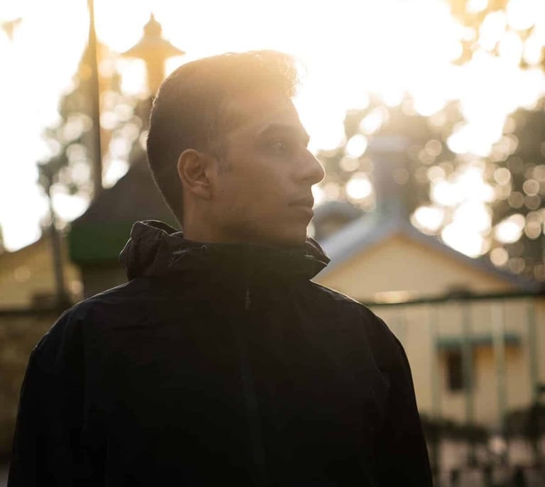Person in dark jacket gazing toward golden-lit historic architecture at dusk.